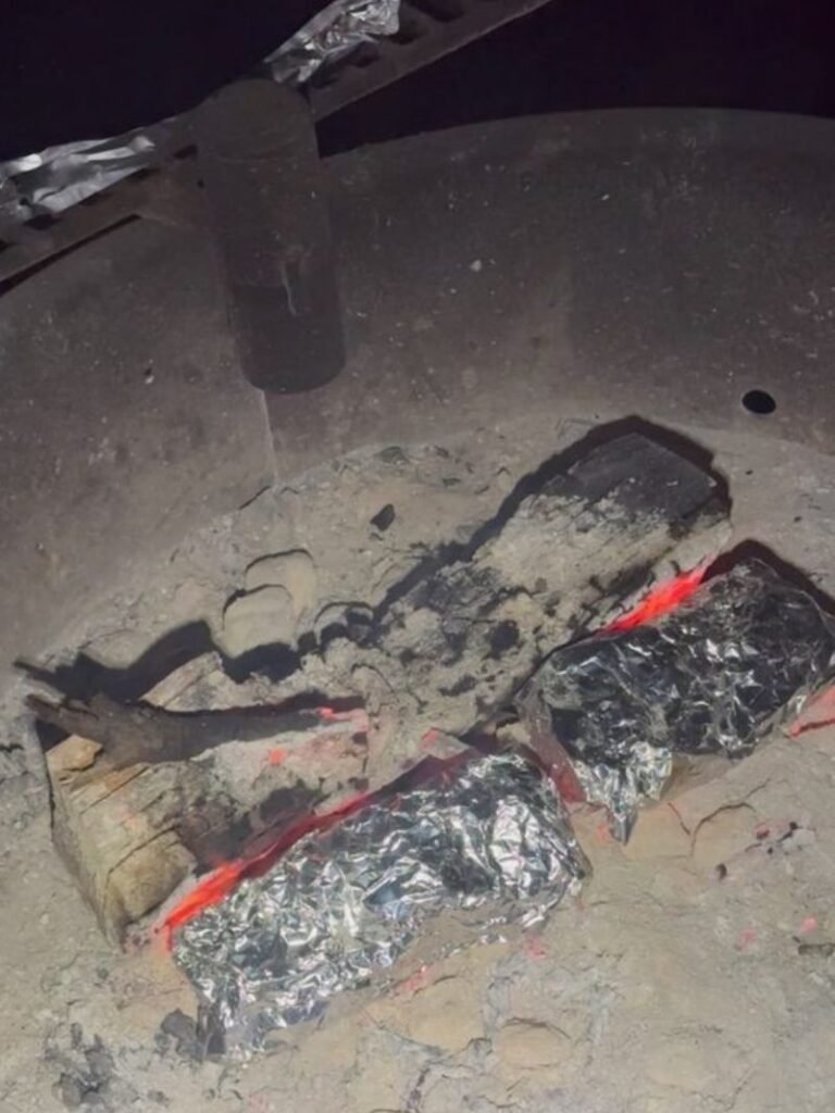Foil-wrapped dinner cooking over campfire coals at night