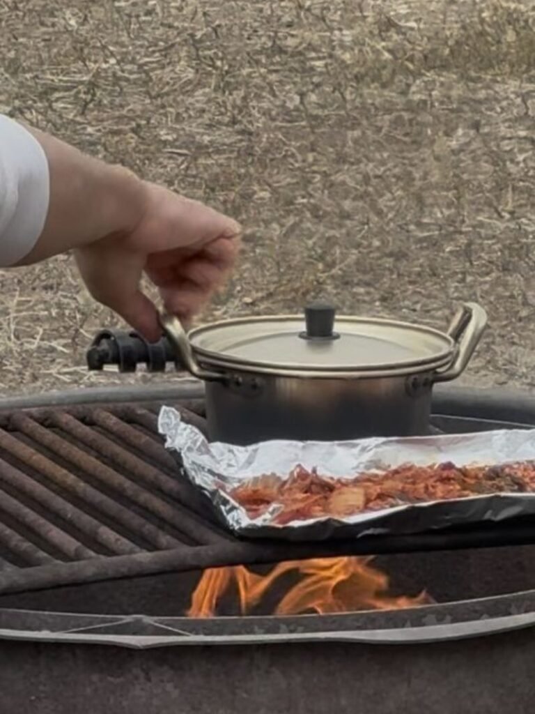 Husband cooking rice and grilled meat over a campfire the morning after car camping