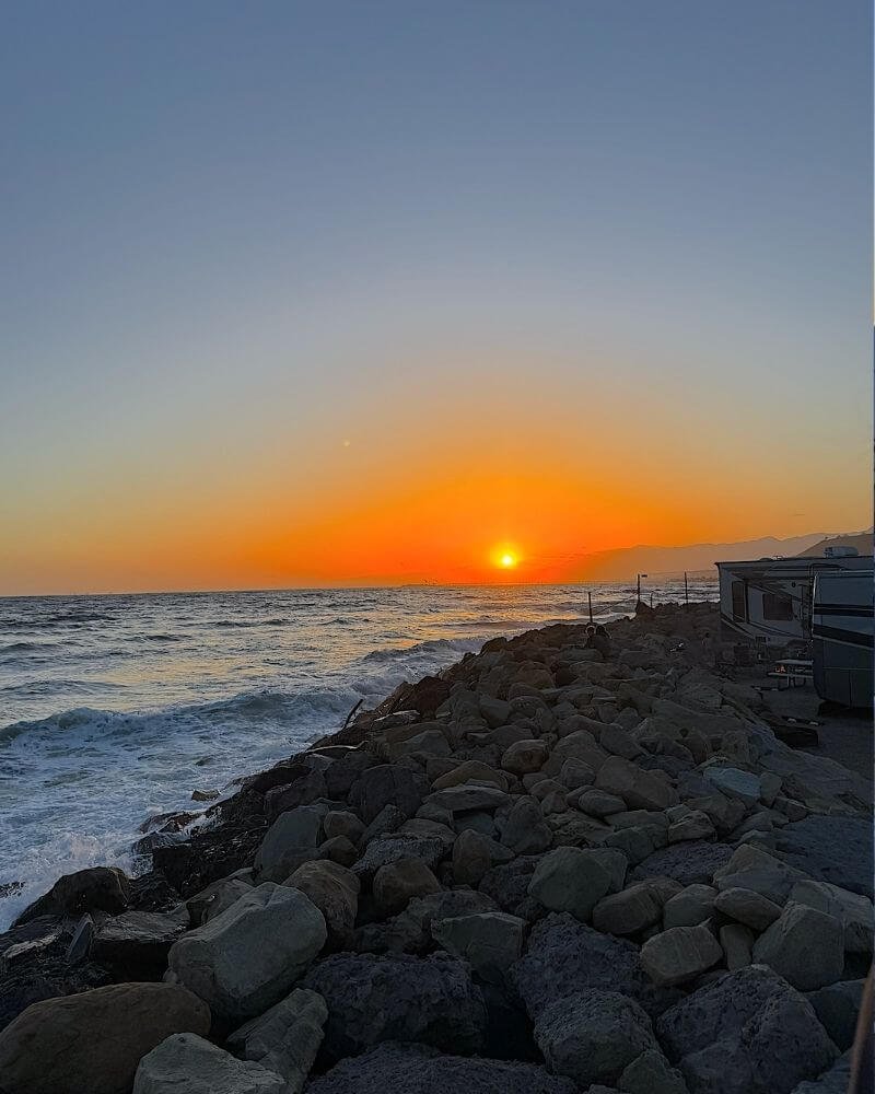 Vibrant orange sunset over crashing ocean waves along the rocky seawall at Hobson Beach