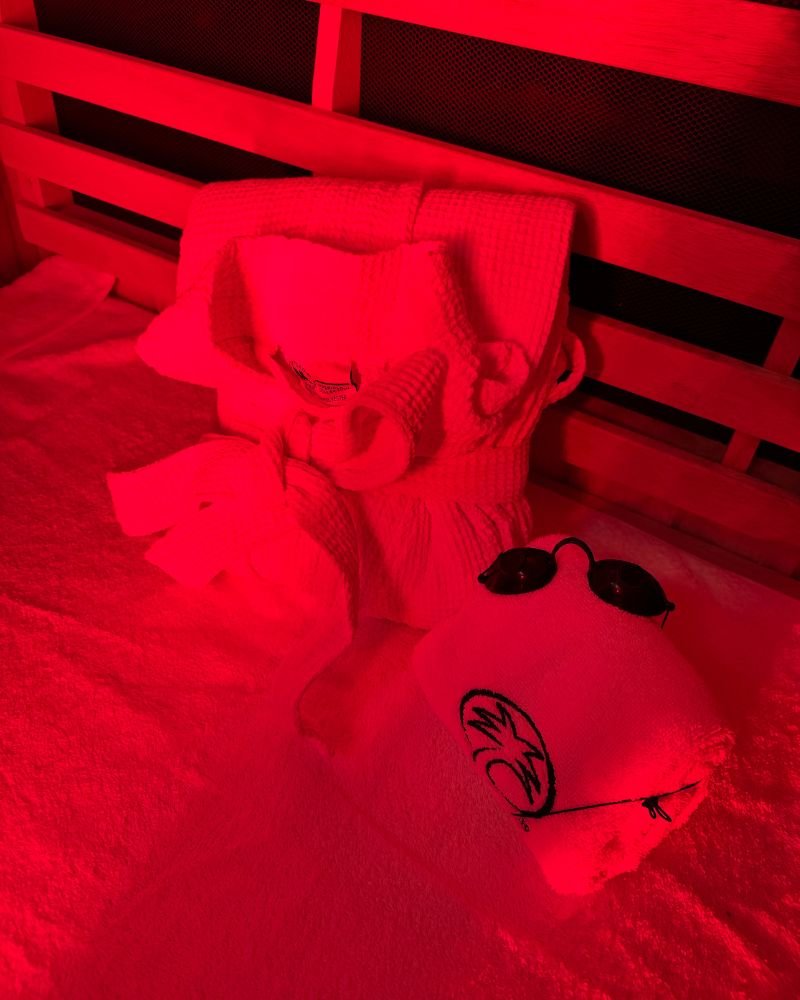 Folded waffle robe, towel, and protective goggles setup inside a red light therapy sauna