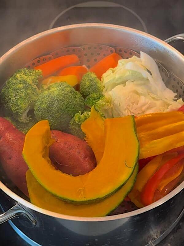 Steaming carrots, cabbage, broccoli, sweet potatoes, and pumpkin in a steamer pot
