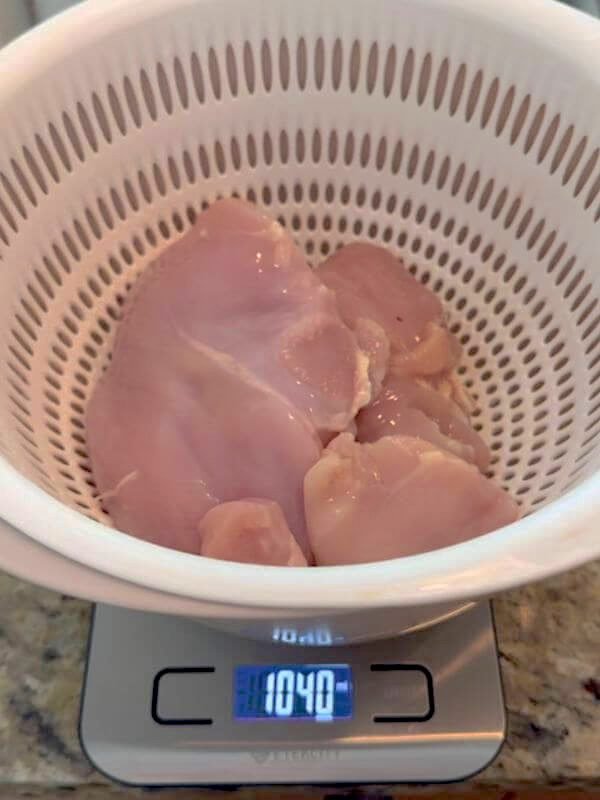 Weighing boneless skinless raw chicken breast on a kitchen scale for homemade dog food recipe