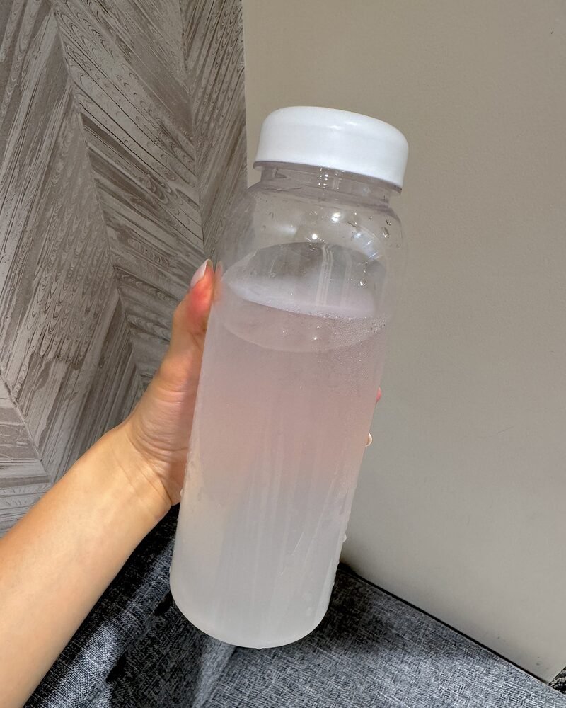 A clear bottle of electrolyte water held up in morning light, the one I use to track how much water to drink after sauna