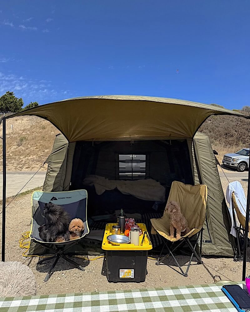 Tent with an awning at a Jalama Beach campsite with two small dogs sitting in camp chairs under blue sky