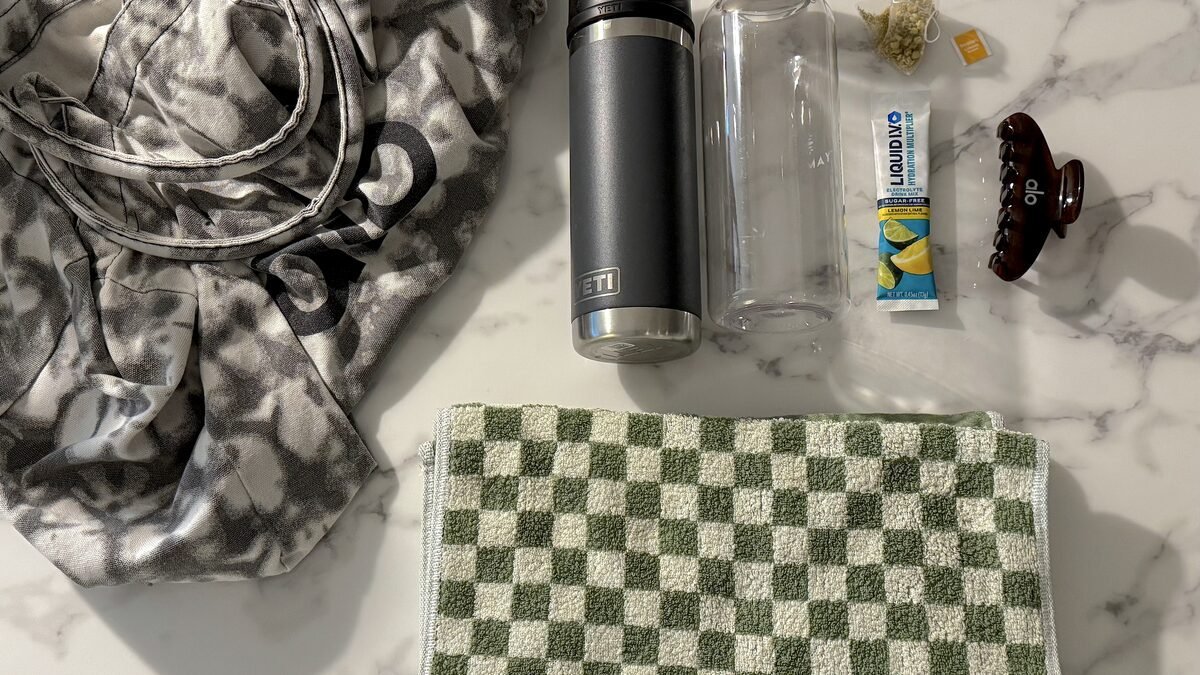 A small bag with two towels, a claw clip, two tumblers and an electrolyte stick laid out to show what to bring to an infrared sauna session