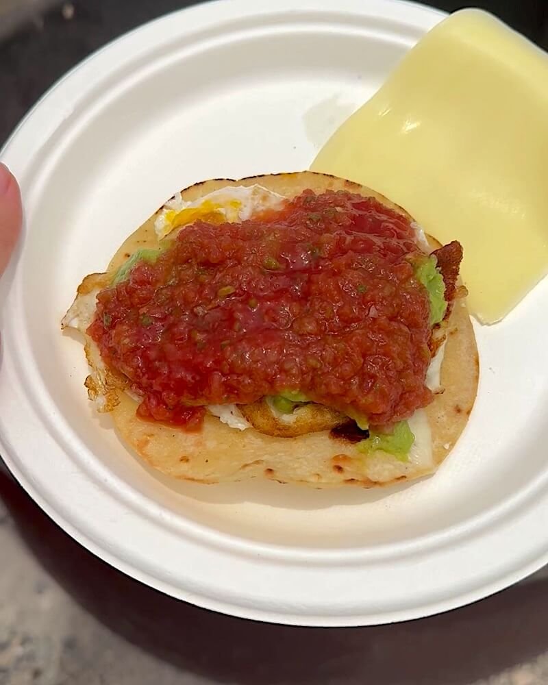 Warm tortilla on a paper plate topped with a fried egg, avocado and a spoonful of red salsa at a campsite
