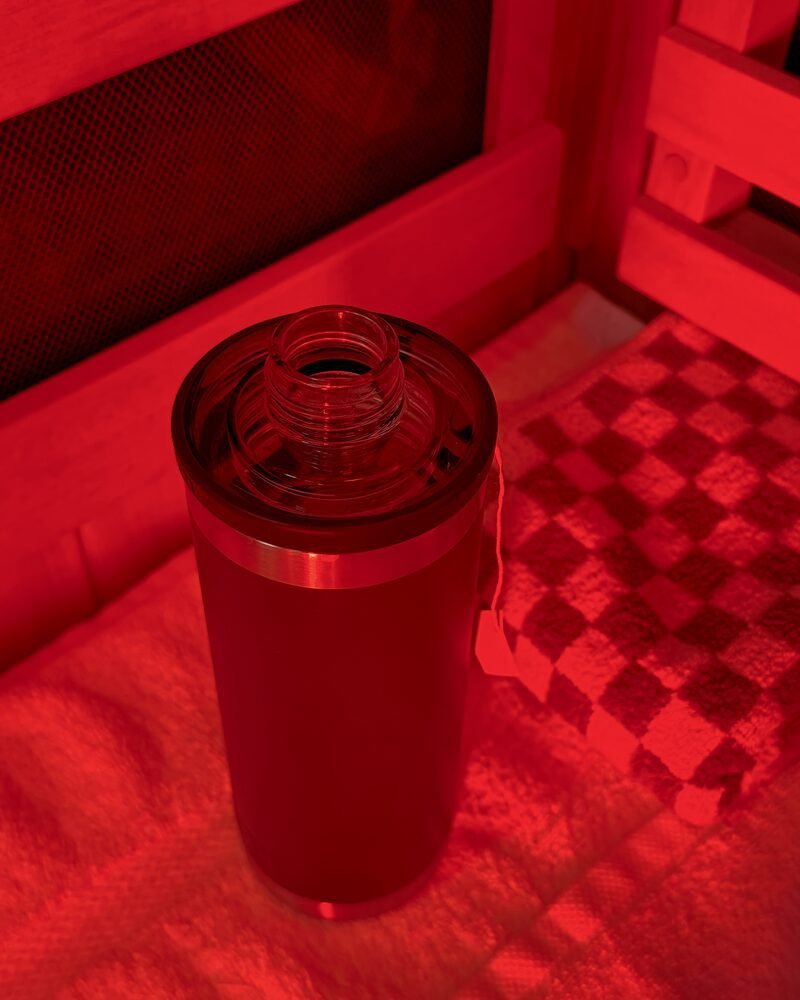 A stainless tumbler and a folded towel on the bench inside the red lit booth