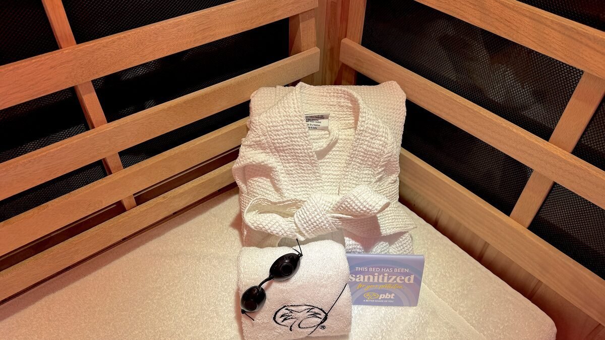 A robe, a folded towel and small dark goggles set out on the bench inside the sauna booth before a session
