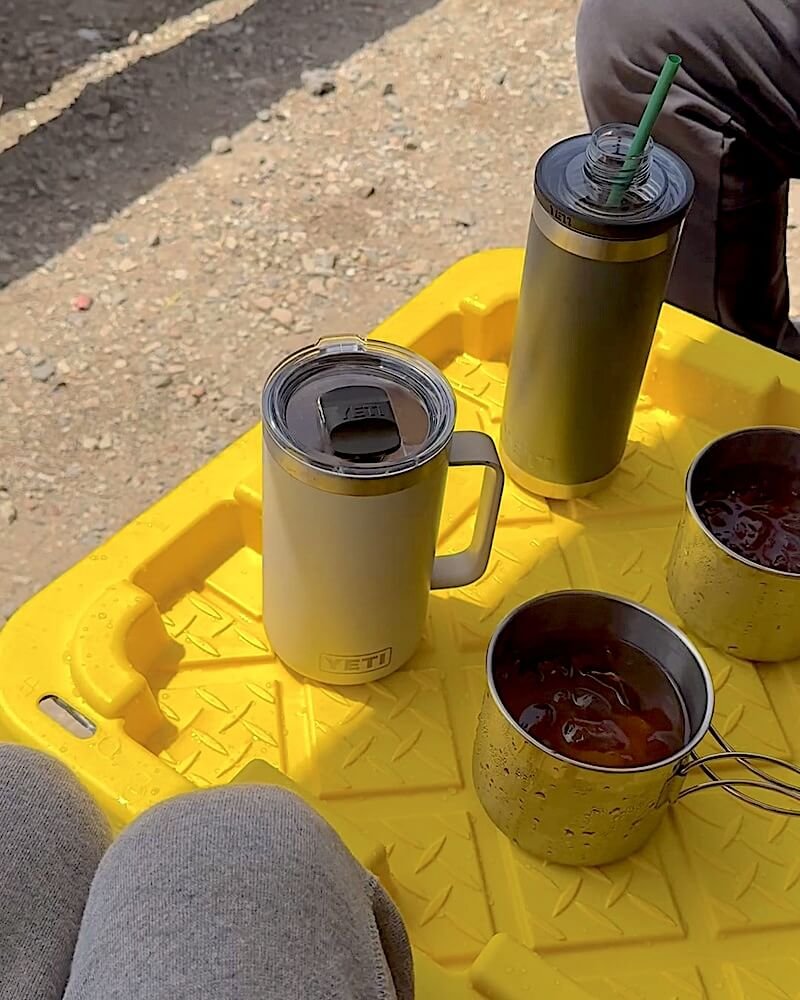 What Is It Like to Camp With No Cell Service? Our Three Days Offline Camp coffee mugs and a tumbler on a yellow folding table during three days without a phone