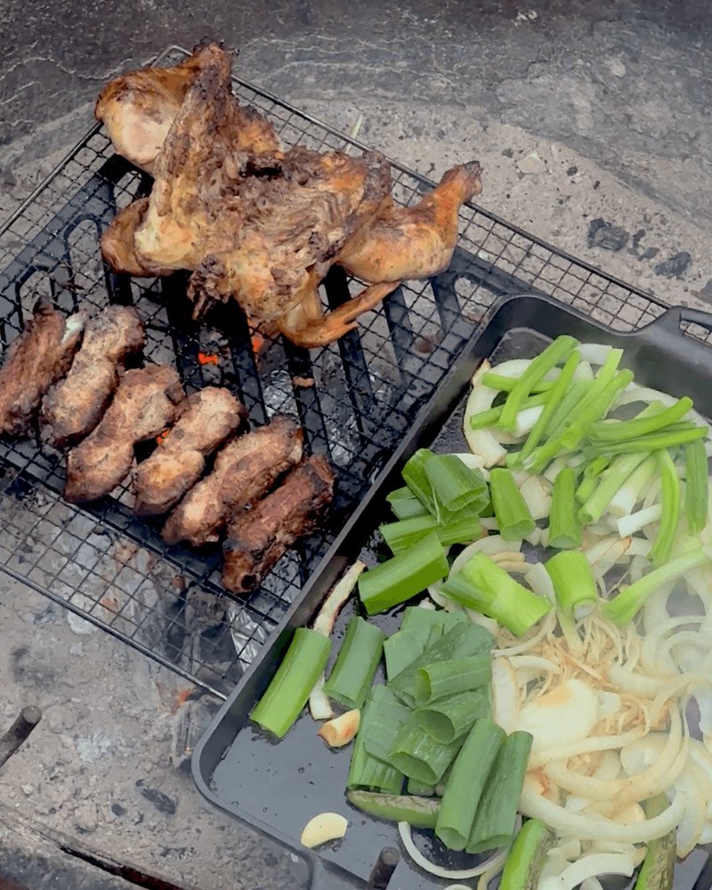 Westside Regional Park Camping With Dogs: What We Wish We'd Known Whole chicken and ribs on a campfire grate next to a pan of green onions and onion at a coastal campsite