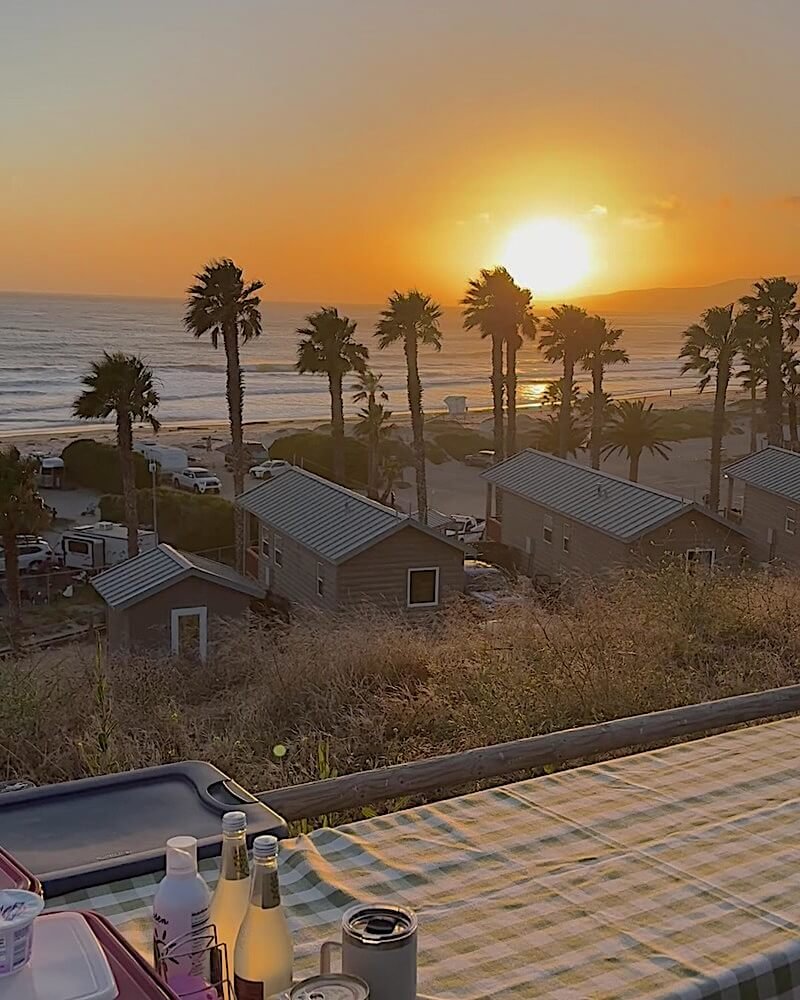 Orange sunset over the ocean framed by tall palm trees above the RVs at Jalama Beach campground