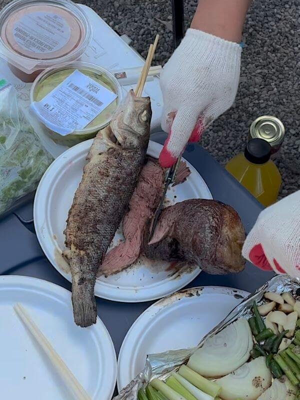 Whole grilled fish and sliced medium-rare steak served with roasted vegetables and Whole Foods sides at beach campsite