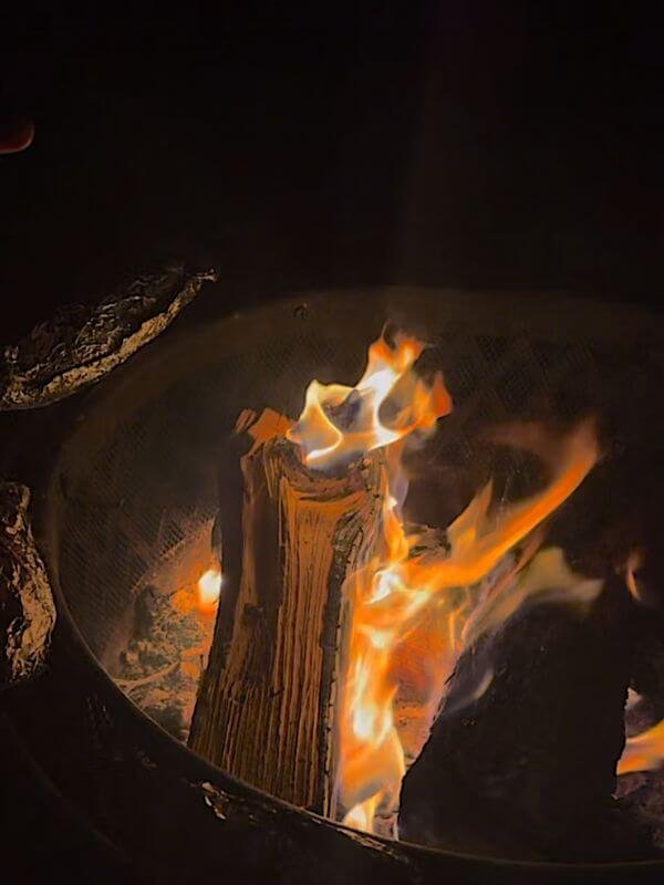 Warm campfire flames glowing inside metal fire ring during cozy evening outdoor trip