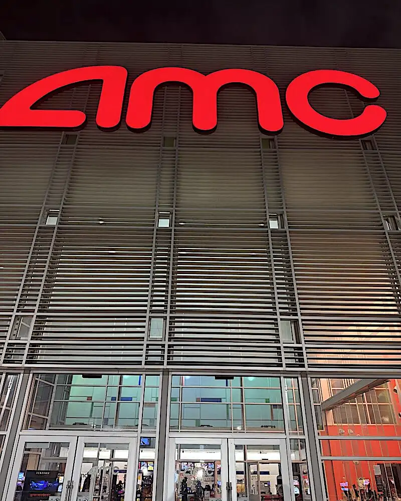 Is Resident Evil 2026 worth watching: the red AMC sign glowing above the glass doors of the theater at night