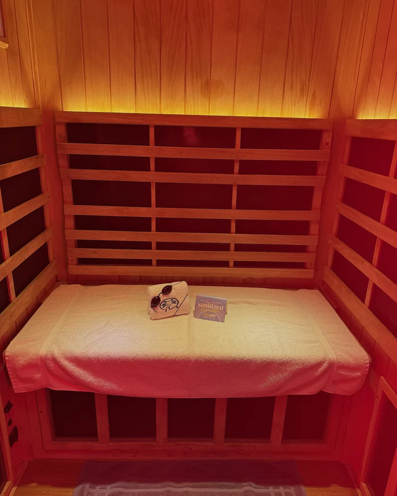 Infrared Sauna Cost: My $69.99 Membership vs Buying One (With Red Light) Infrared sauna cost: inside the wooden full spectrum booth with the red light on, a towel on the bench and goggles waiting