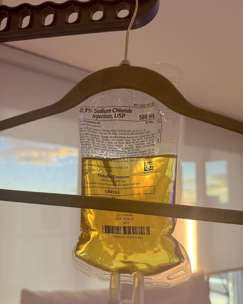 How Long Does an IV Drip Take? My 90-Minute vs 6-Hour Drips How long does an IV drip take: a 500 mL IV bag of yellow vitamin fluid hanging from a clothes hanger by the window at sunset