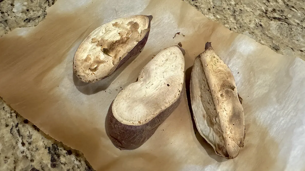 Halved Korean sweet potatoes with purple skin and pale yellow flesh on parchment paper on the kitchen counter