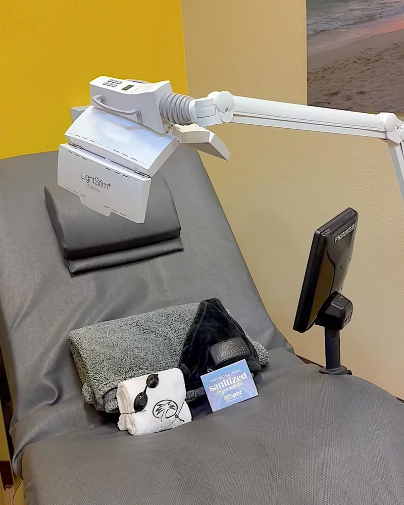 Tanning Salon Red Light Therapy: My Honest Routine After 10+ Face Sessions White LED face panel on a swing arm above a gray massage bed with goggles and a towel