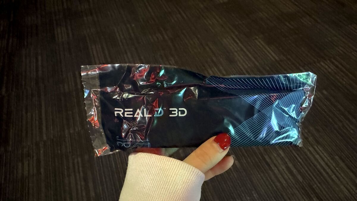 I Almost Skipped The Nightmare Before Christmas 3D. One Scene Changed My Mind Hand holding a sealed RealD 3D glasses package in a movie theater hallway