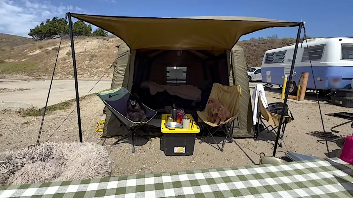 Air Tent Setup Mistakes Air tent with its awning propped on poles and guy lines staked into the ground at a beach campsite with a vintage trailer parked behind