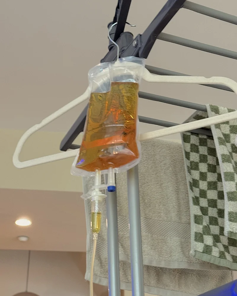 What Is in an IV Drip? Every Ingredient in My At-Home IV Bag (and Why It Turned Yellow) An orange tinted IV bag hanging from a clothes hanger on a drying rack