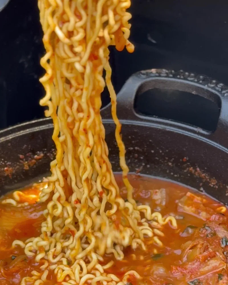 Camping Food List: What We Actually Ate in 3 Nights (Korean Dinners, Drinks, and the Dogs' Food) Ramen noodles lifted out of red kimchi stew in a black pot at camp