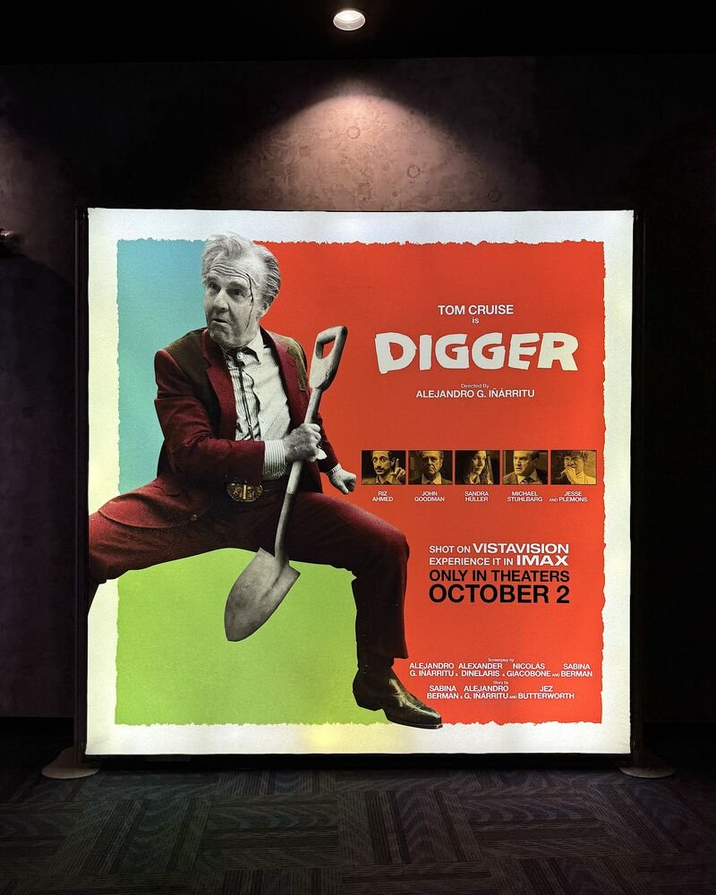 Tom Cruise as Digger with white hair and a red suit on a lit poster display inside an AMC theater