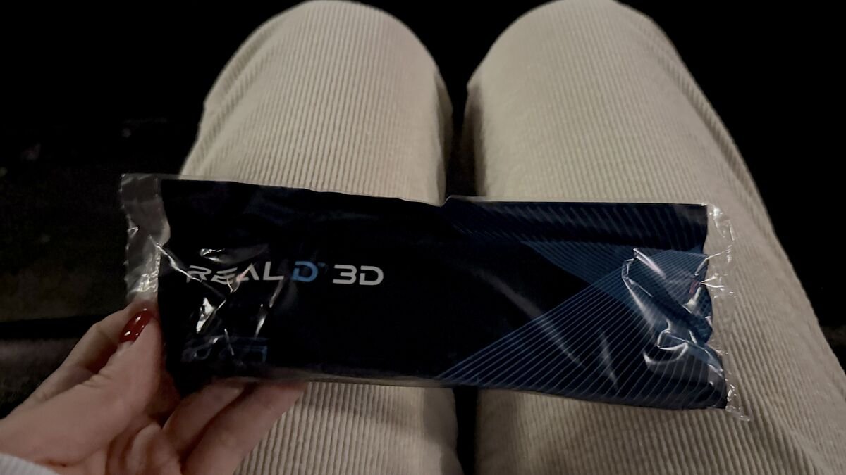 I Almost Skipped The Nightmare Before Christmas 3D. One Scene Changed My Mind Sealed RealD 3D glasses package held over a lap in a dark theater seat