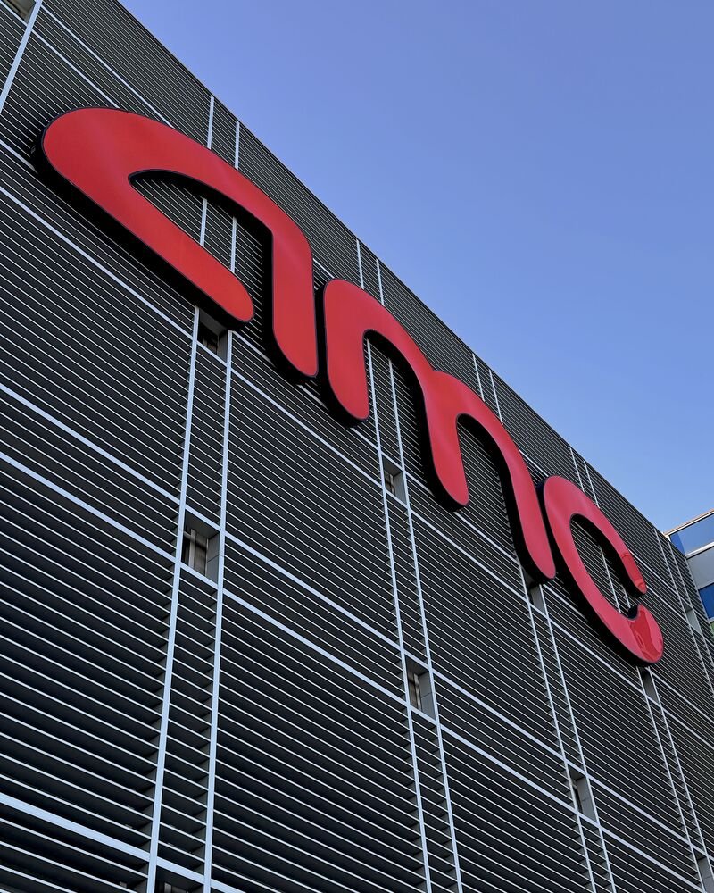 Red AMC sign on the side of a movie theater against a blue sky
