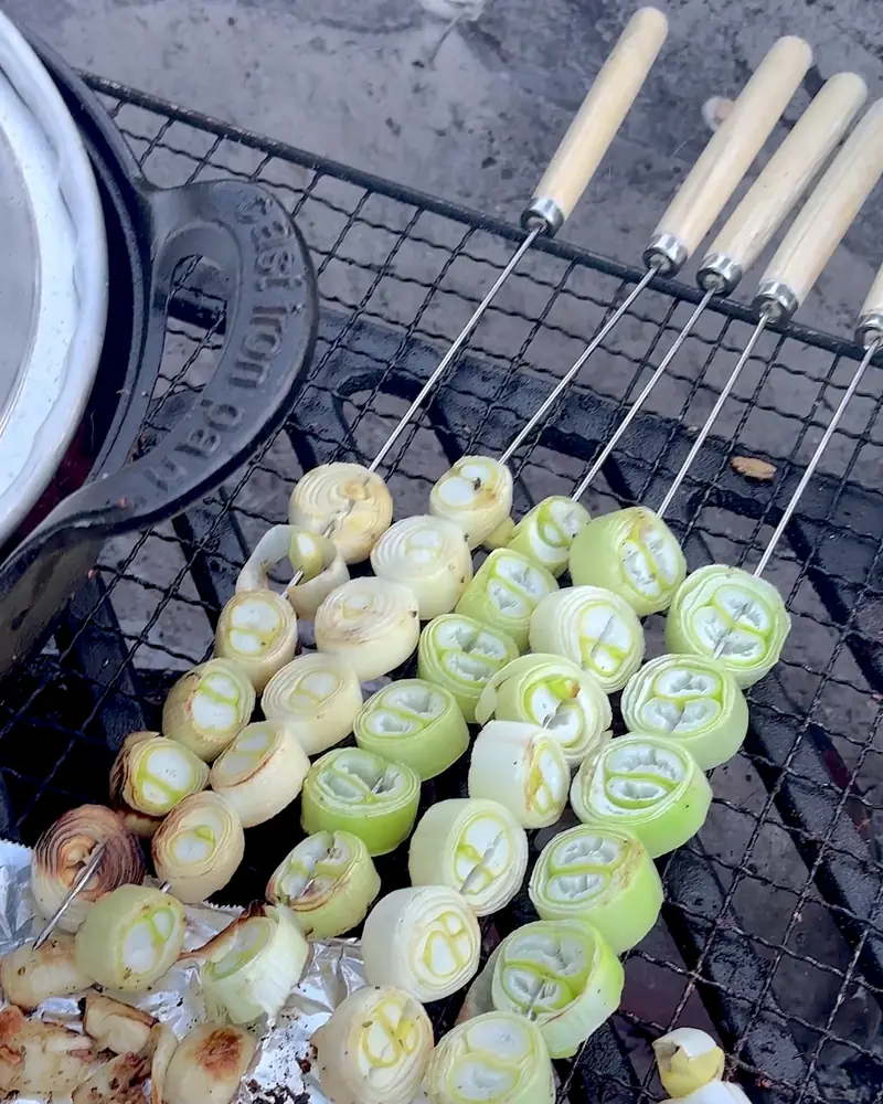 Cooking on a Fire Pit at Camp (6 Things We Made, From Lamb Chops to Pork Belly) Thick slices of green onion threaded on wooden skewers grilling on the campfire grate