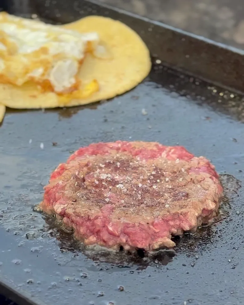Easy Camping Breakfast: 4 Campfire Griddle Meals We Made (Nothing Prepped at Home) Smashed beef patty sizzling on a cast iron griddle next to a tortilla