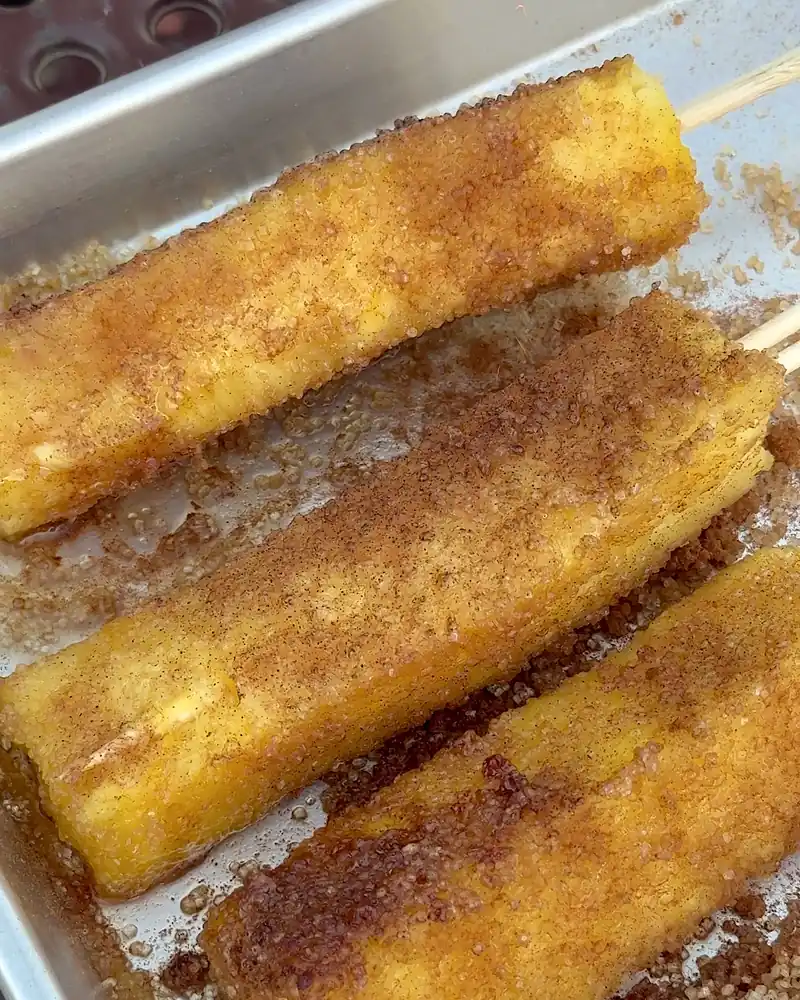 Cooking on a Fire Pit at Camp (6 Things We Made, From Lamb Chops to Pork Belly) Pineapple spears on skewers coated in sugar and cinnamon on a metal tray