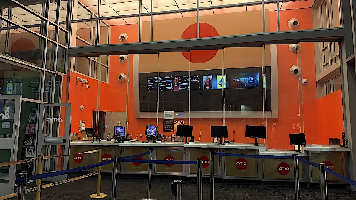 Empty AMC ticket counter in front of a bright orange wall with rope lines and screens