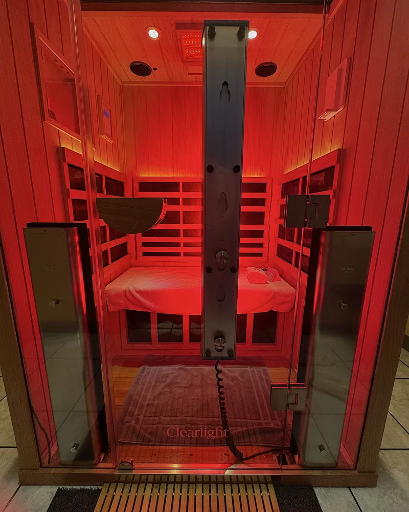 Infrared Sauna Cost: My $69.99 Membership vs Buying One (With Red Light) The full spectrum infrared booth behind its glass door with the red light on and the Clearlight logo on the glass