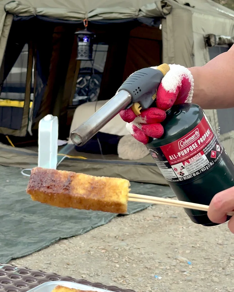 Cooking on a Fire Pit at Camp (6 Things We Made, From Lamb Chops to Pork Belly) Caramelizing a cinnamon sugar pineapple skewer with a handheld propane torch at camp