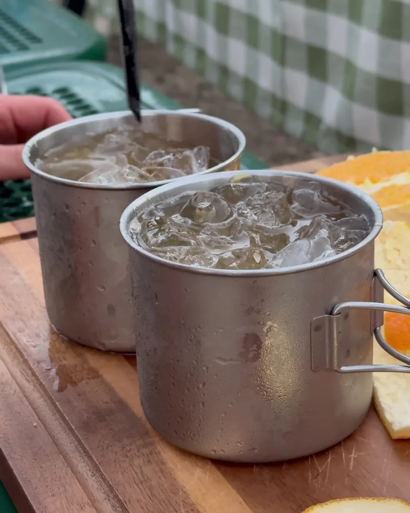 Camping Food List: What We Actually Ate in 3 Nights (Korean Dinners, Drinks, and the Dogs' Food) Two stainless steel camp mugs of iced whiskey and ginger beer on a cutting board