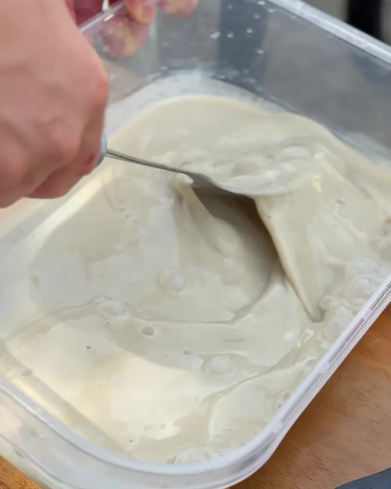 Easy Camping Breakfast: 4 Campfire Griddle Meals We Made (Nothing Prepped at Home) Hand stirring French toast batter with a spoon in a clear plastic container