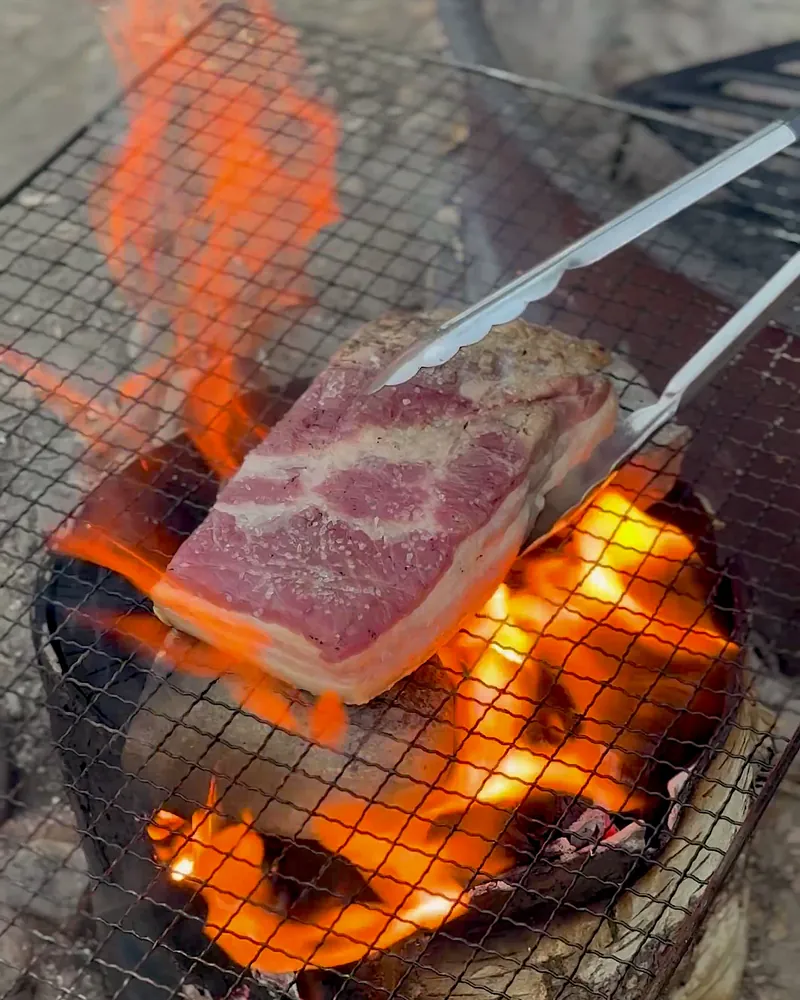 Cooking on a Fire Pit at Camp (6 Things We Made, From Lamb Chops to Pork Belly) A whole slab of pork belly seasoned with salt and pepper over high flames on a round wire rack