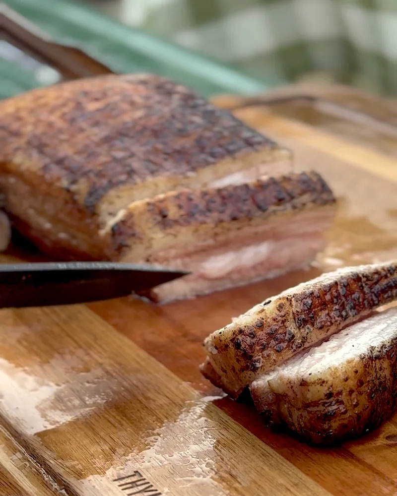 Cooking on a Fire Pit at Camp (6 Things We Made, From Lamb Chops to Pork Belly) Slicing the fire-roasted pork belly on a wooden cutting board